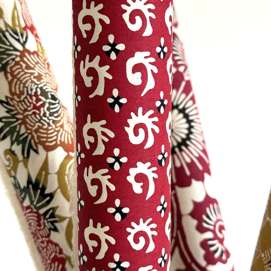 A Japanese stencil-dyed patterned paper with a repeat pattern in white on a deep rich red background. Close-up