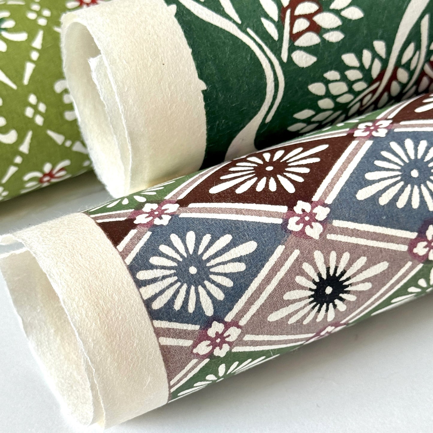 A Japanese stencil-dyed patterned paper with a repeat diamond floral pattern in blue, taupe, green and brown. Close-up rolled