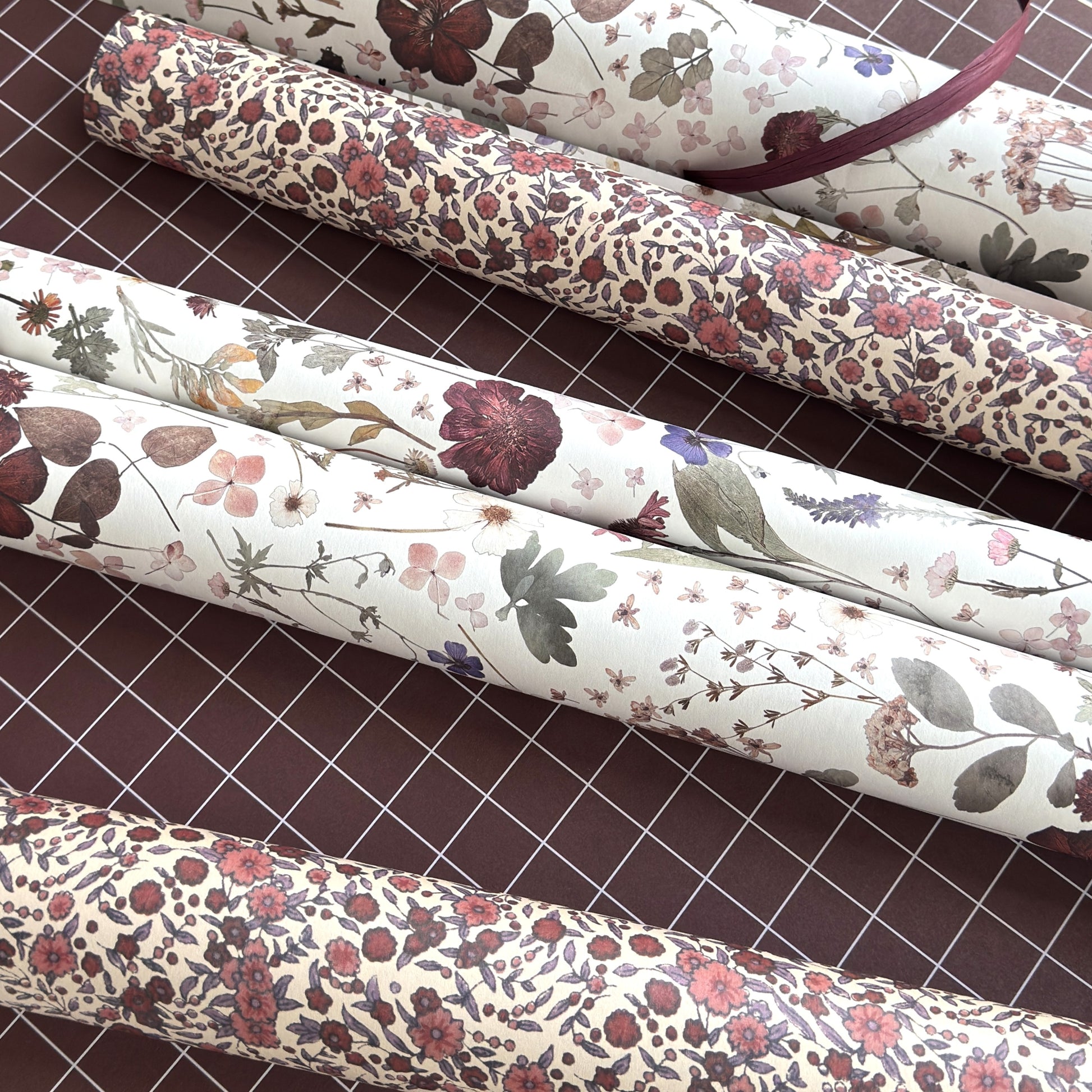 a sheet of wrapping paper with a pretty floral design of pressed flowers on one side, a small scale rose pattern on the other, both on a white background. Pictured rolled
