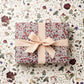 a sheet of wrapping paper with a pretty floral small scale rose design in pink and purple. wrapped with a bow