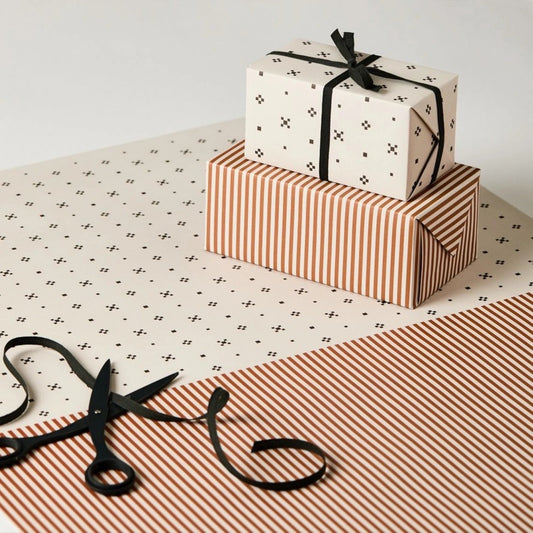 a sheet of wrapping paper with a split design, the top half has little black tile design on white and the bottom half a narrow stripe in cinnamon and white.