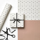 a sheet of wrapping paper with a split design, the top half has little black tile design on white and the bottom half a narrow stripe in cinnamon and white.