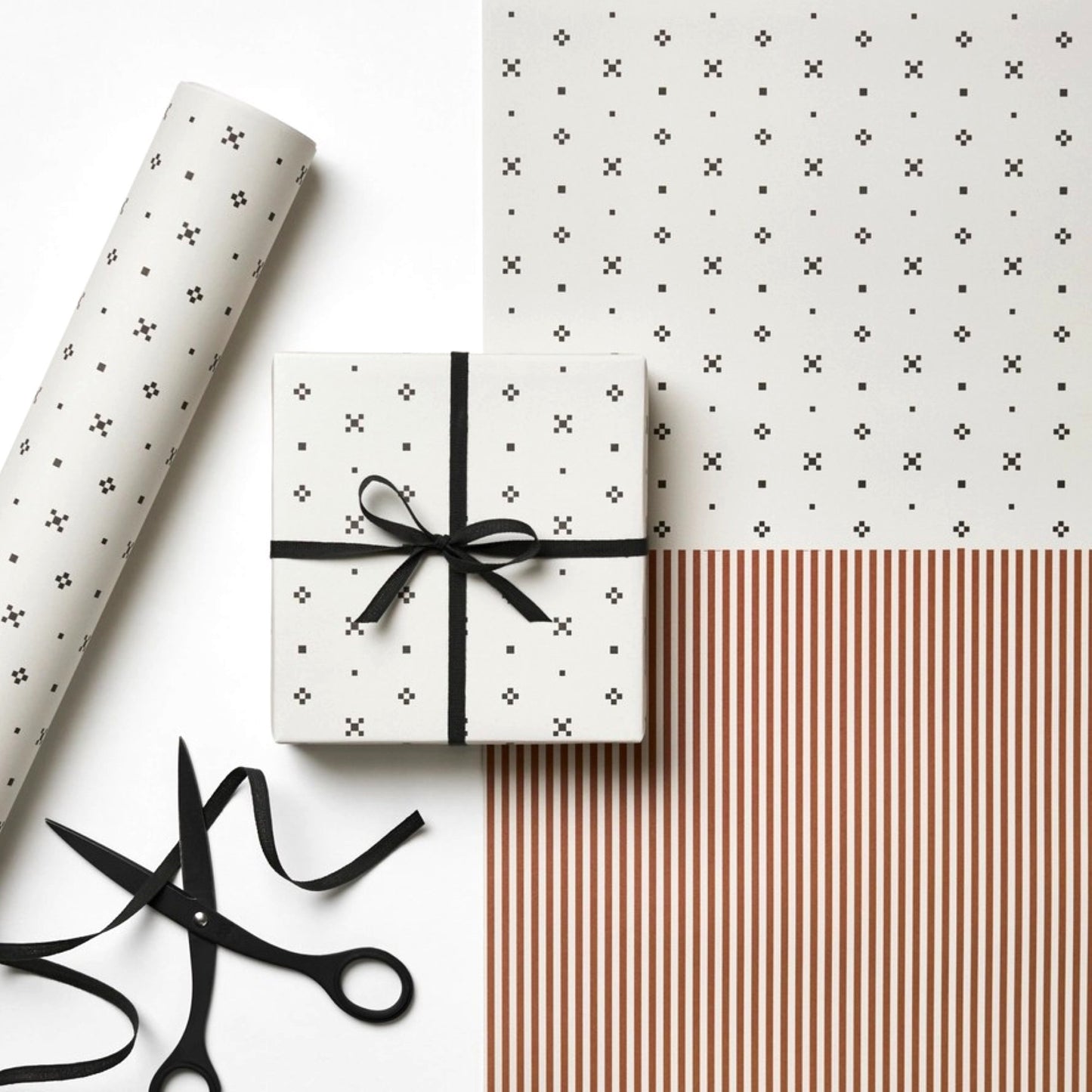a sheet of wrapping paper with a split design, the top half has little black tile design on white and the bottom half a narrow stripe in cinnamon and white.
