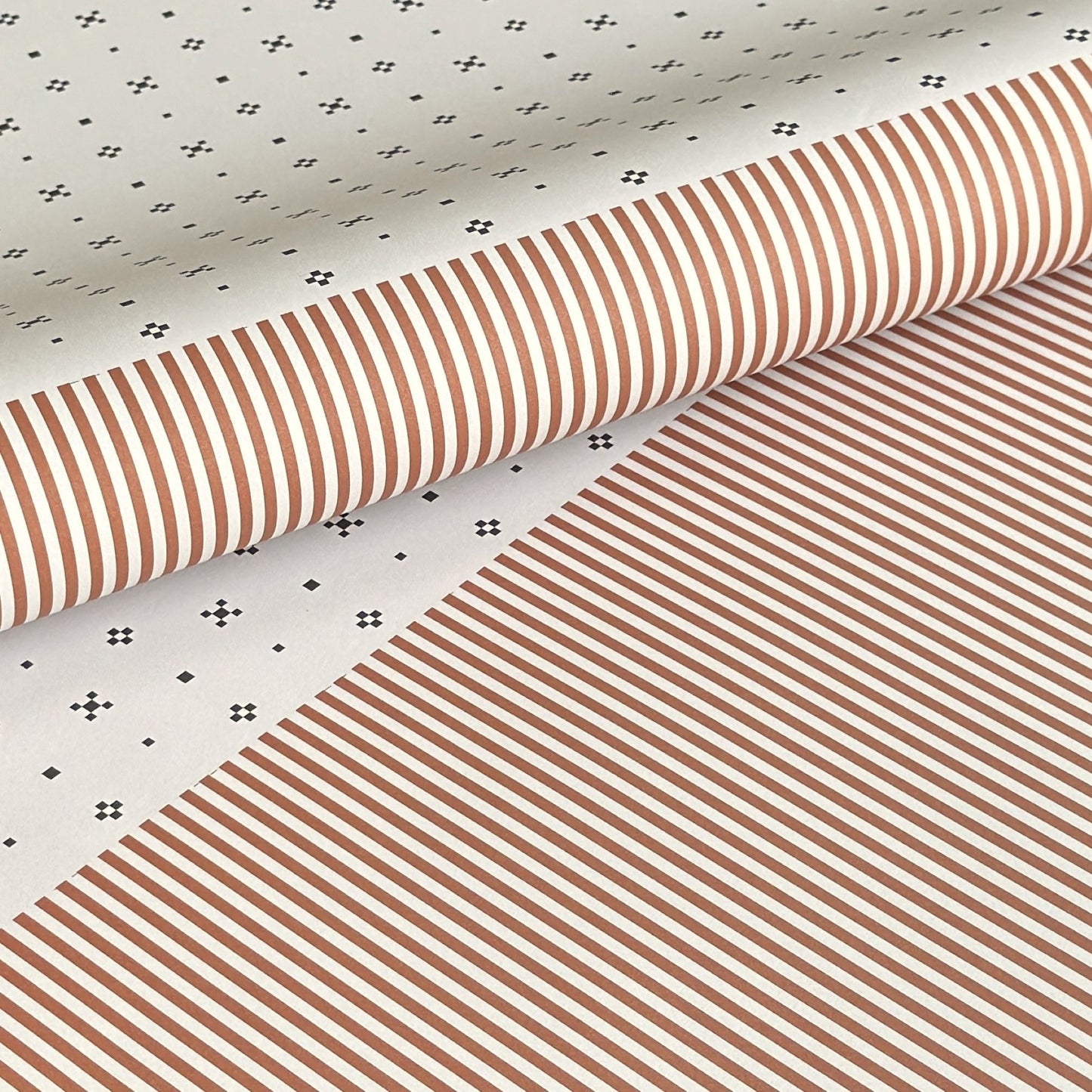 a sheet of wrapping paper with a split design, the top half has little black tile design on white and the bottom half a narrow stripe in cinnamon and white.