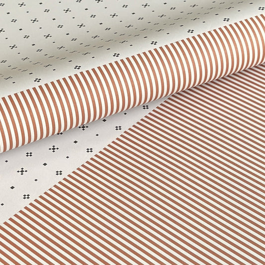 a sheet of wrapping paper with a split design, the top half has little black tile design on white and the bottom half a narrow stripe in cinnamon and white.
