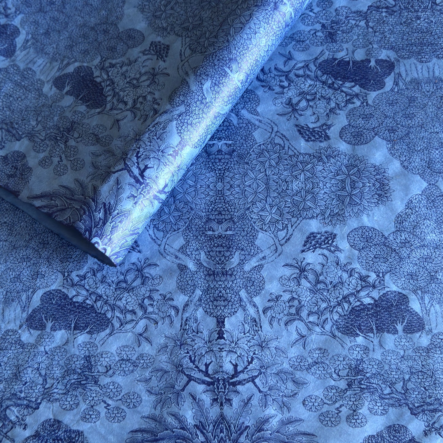 Detailed pattern of trees and flowers in dark blue screen-printed by hand on a blue lokta paper.