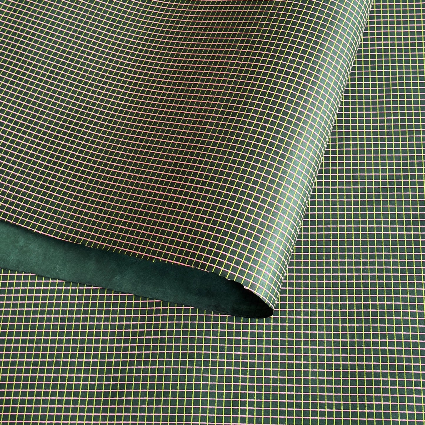 a sheet of Nepalese lokta paper with a lime green and pink grid pattern on dark green handmade paper