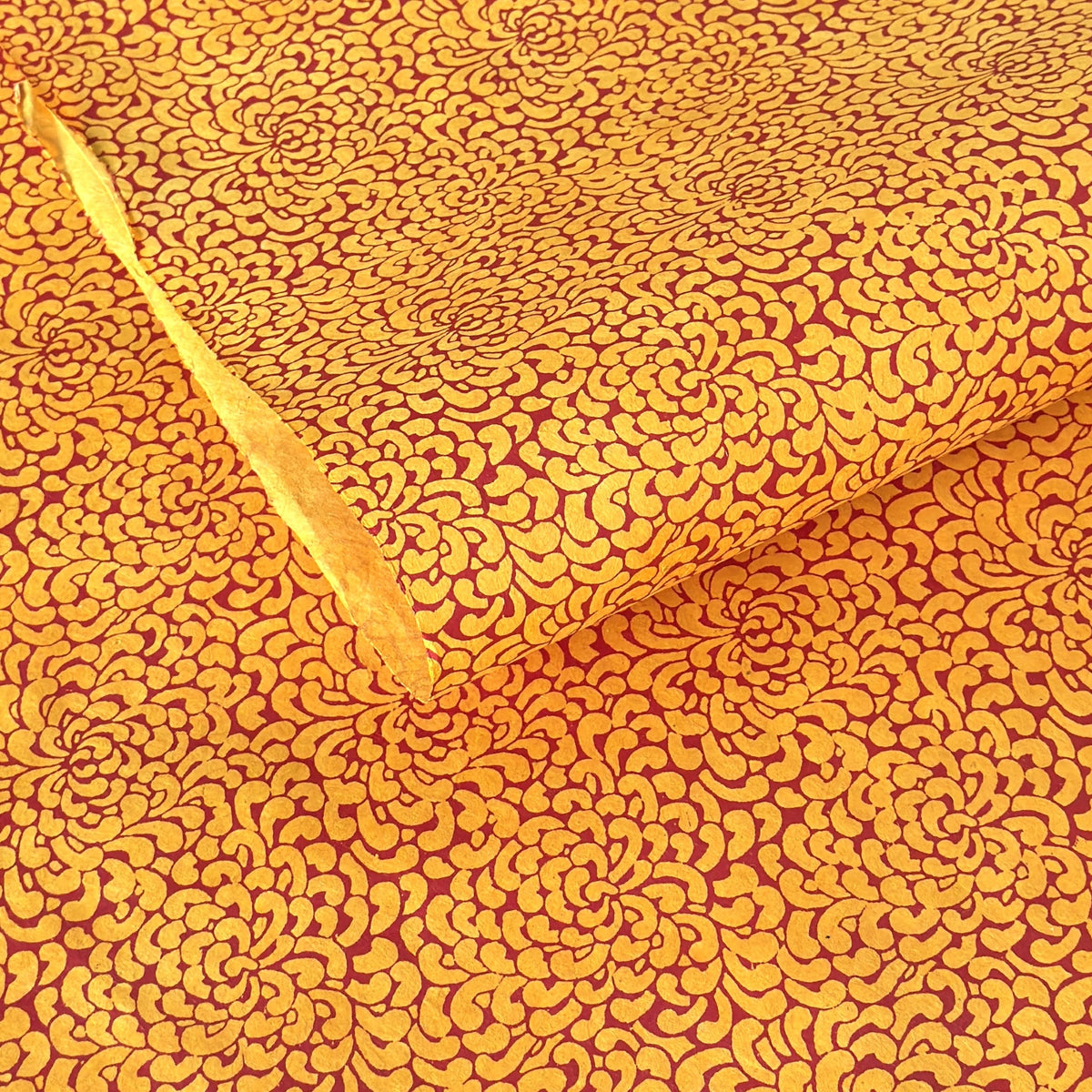 a sheet of screen printed Nepalese lokta paper with a repeat floral design in dark orange on an amber yellow lokta paper 