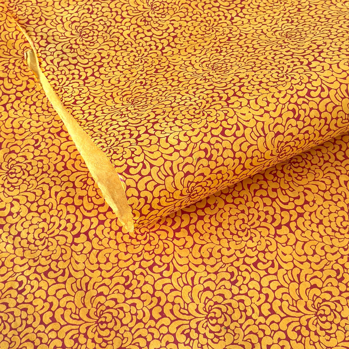 a sheet of screen printed Nepalese lokta paper with a repeat floral design in dark orange on an amber yellow lokta paper 