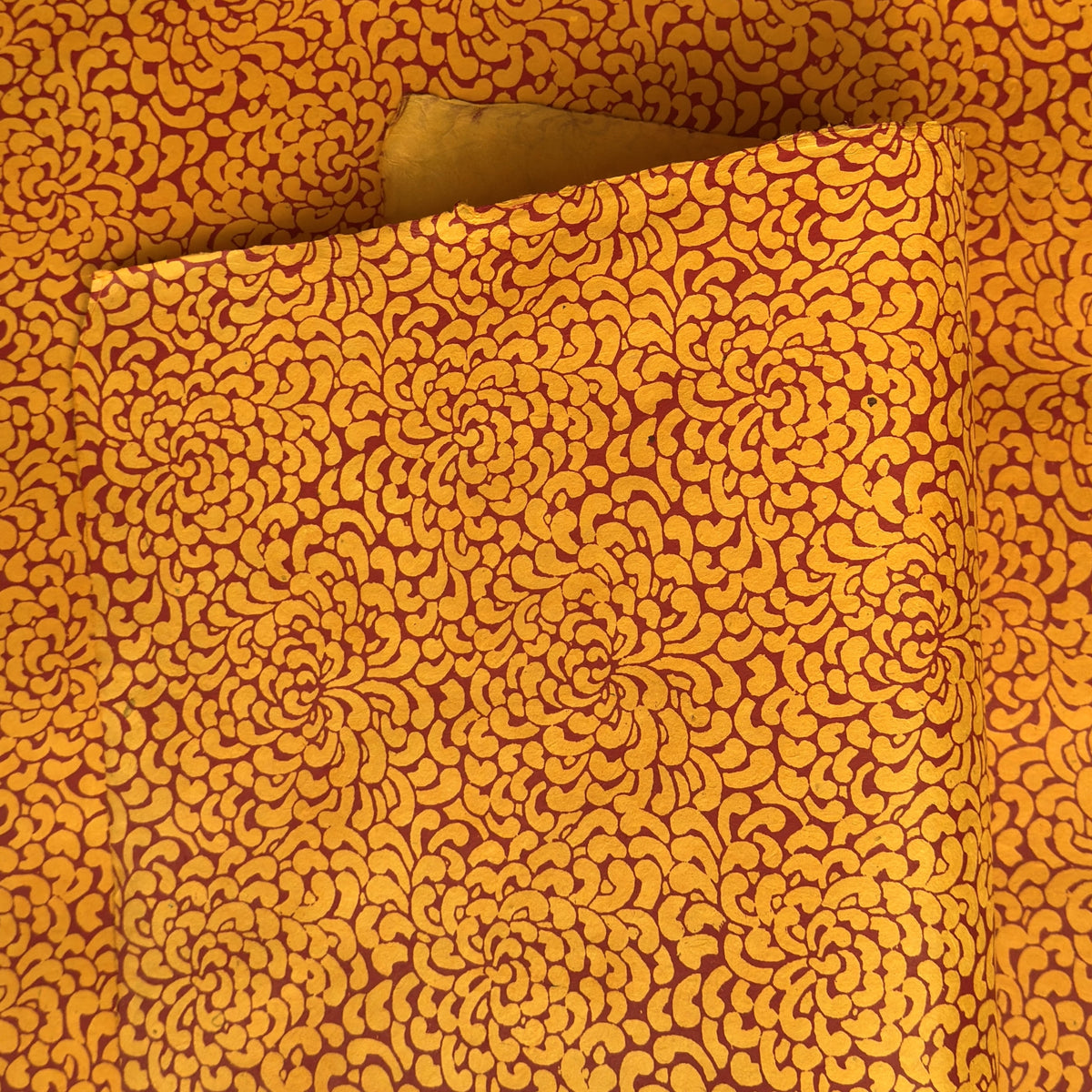 a sheet of screen printed Nepalese lokta paper with a repeat floral design in dark orange on an amber yellow lokta paper 