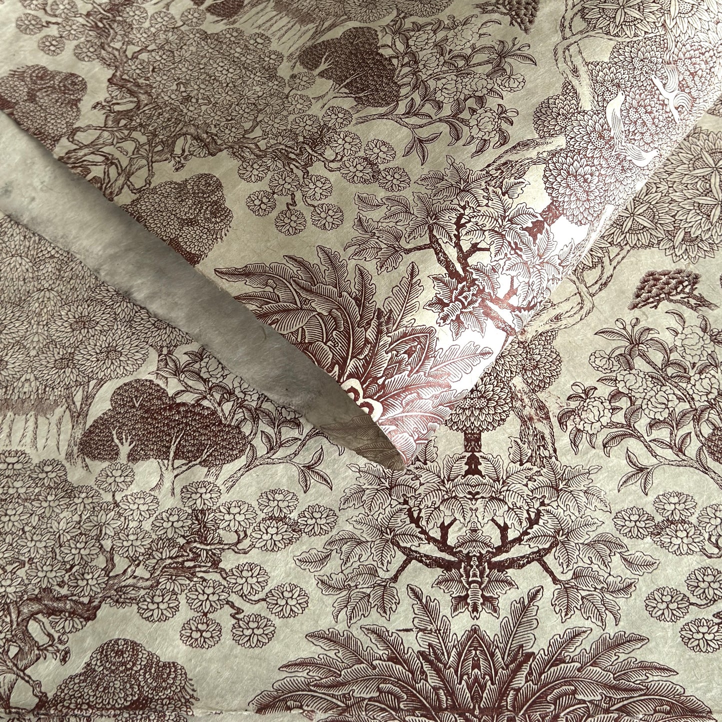 A sheet of Nepalese handprinted Lokta paper with a detailed pattern of trees and flowers in sepia on an ecru base.