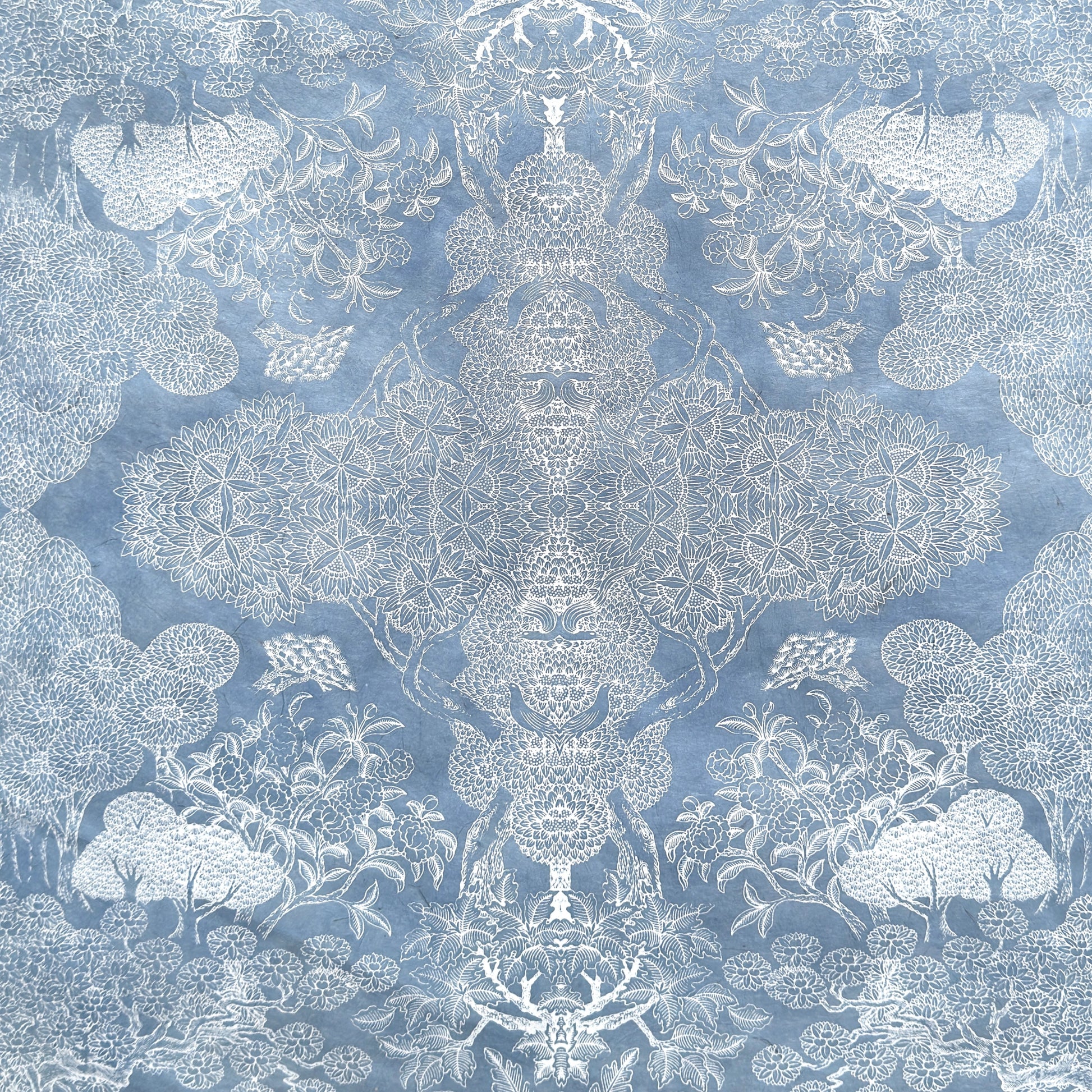 a sheet of Nepalese lokta paper in sky blue with a detailed pattern of trees and flowers screen printed in white