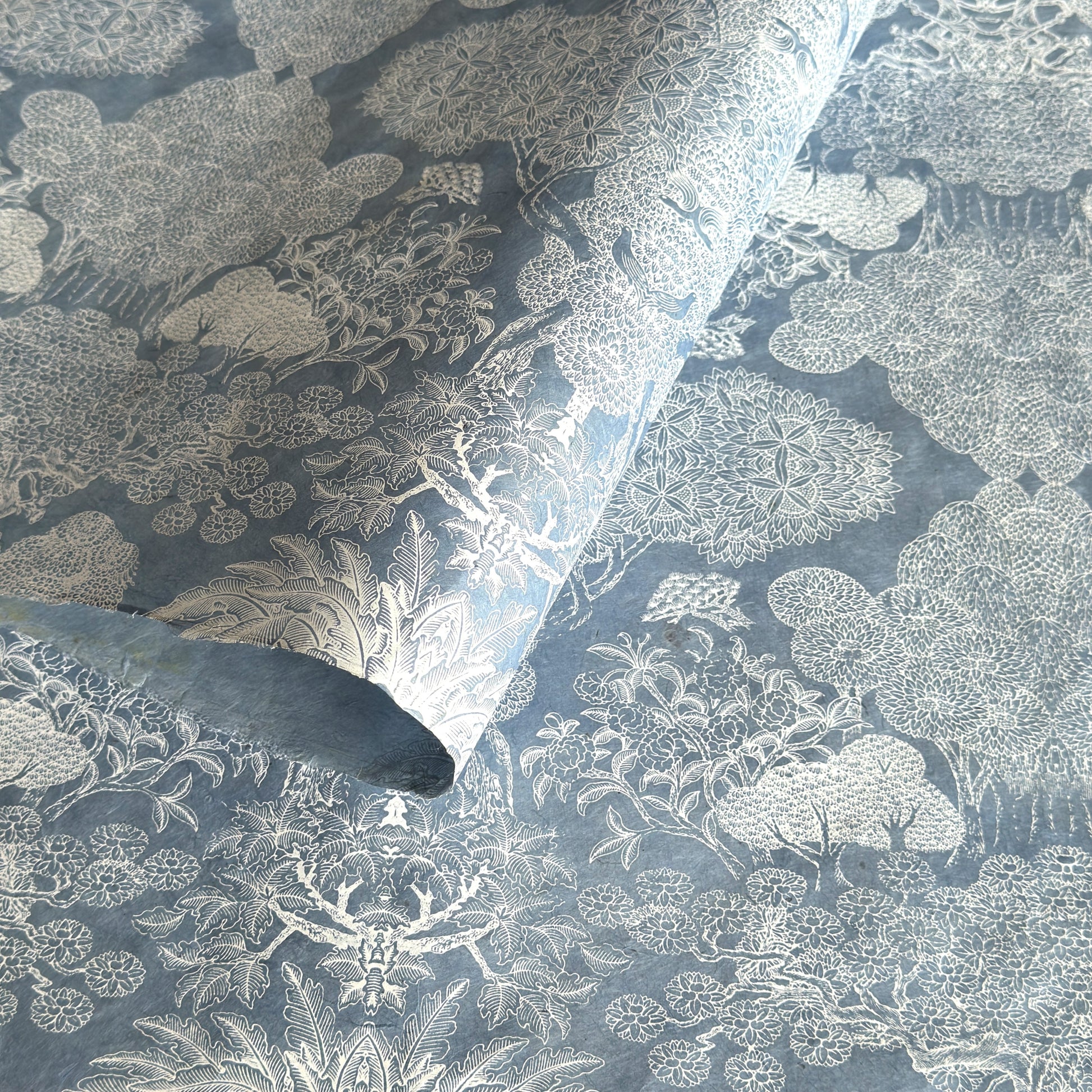 a sheet of Nepalese lokta paper in sky blue with a detailed pattern of trees and flowers screen printed in white