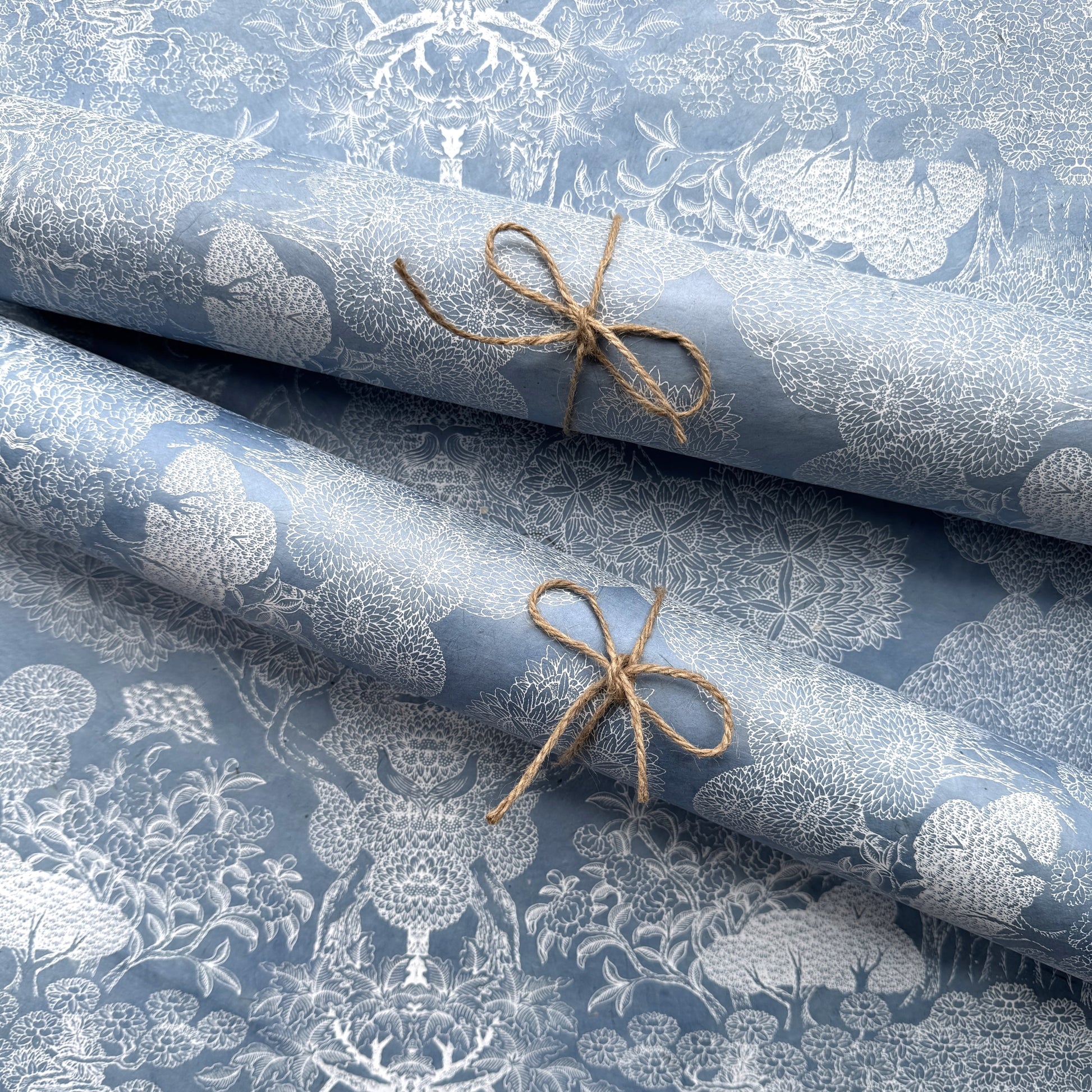 a sheet of Nepalese lokta paper in sky blue with a detailed pattern of trees and flowers screen printed in white