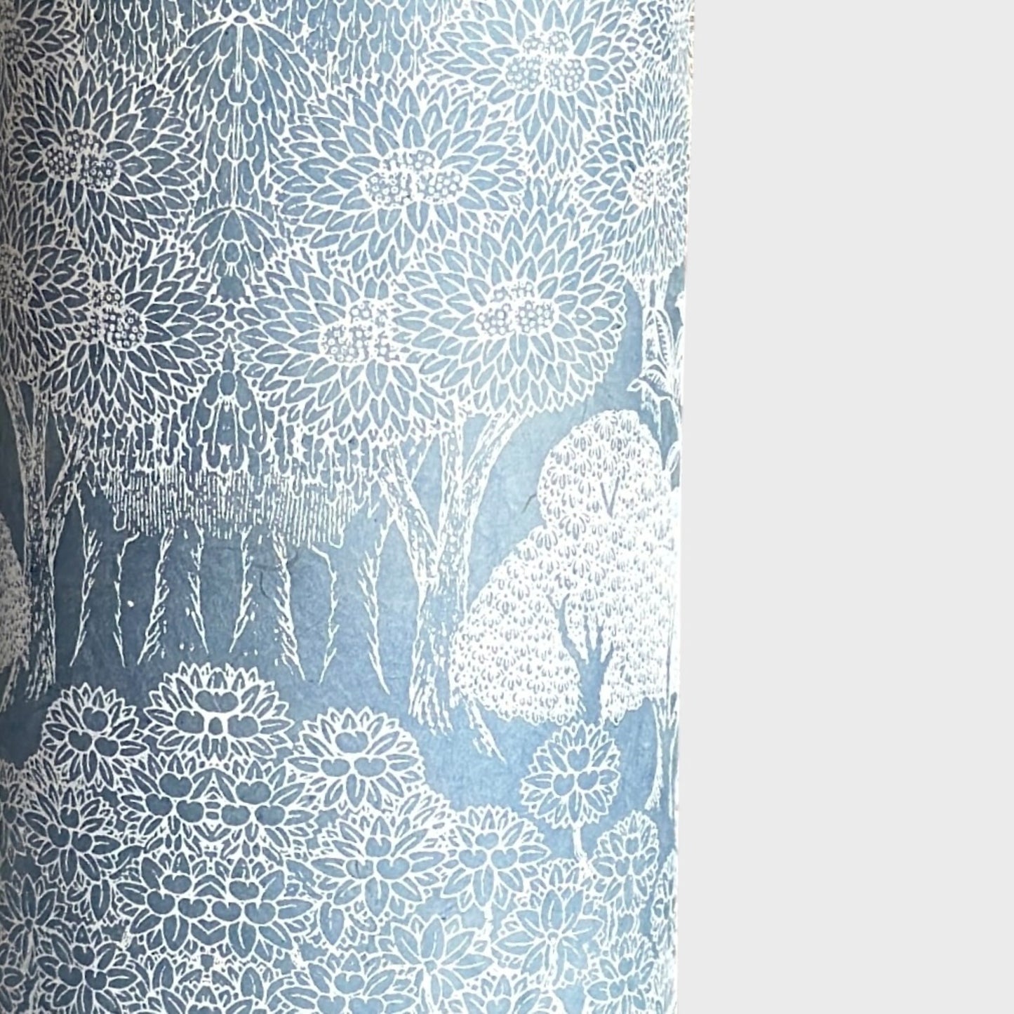 a sheet of Nepalese lokta paper in sky blue with a detailed pattern of trees and flowers screen printed in white