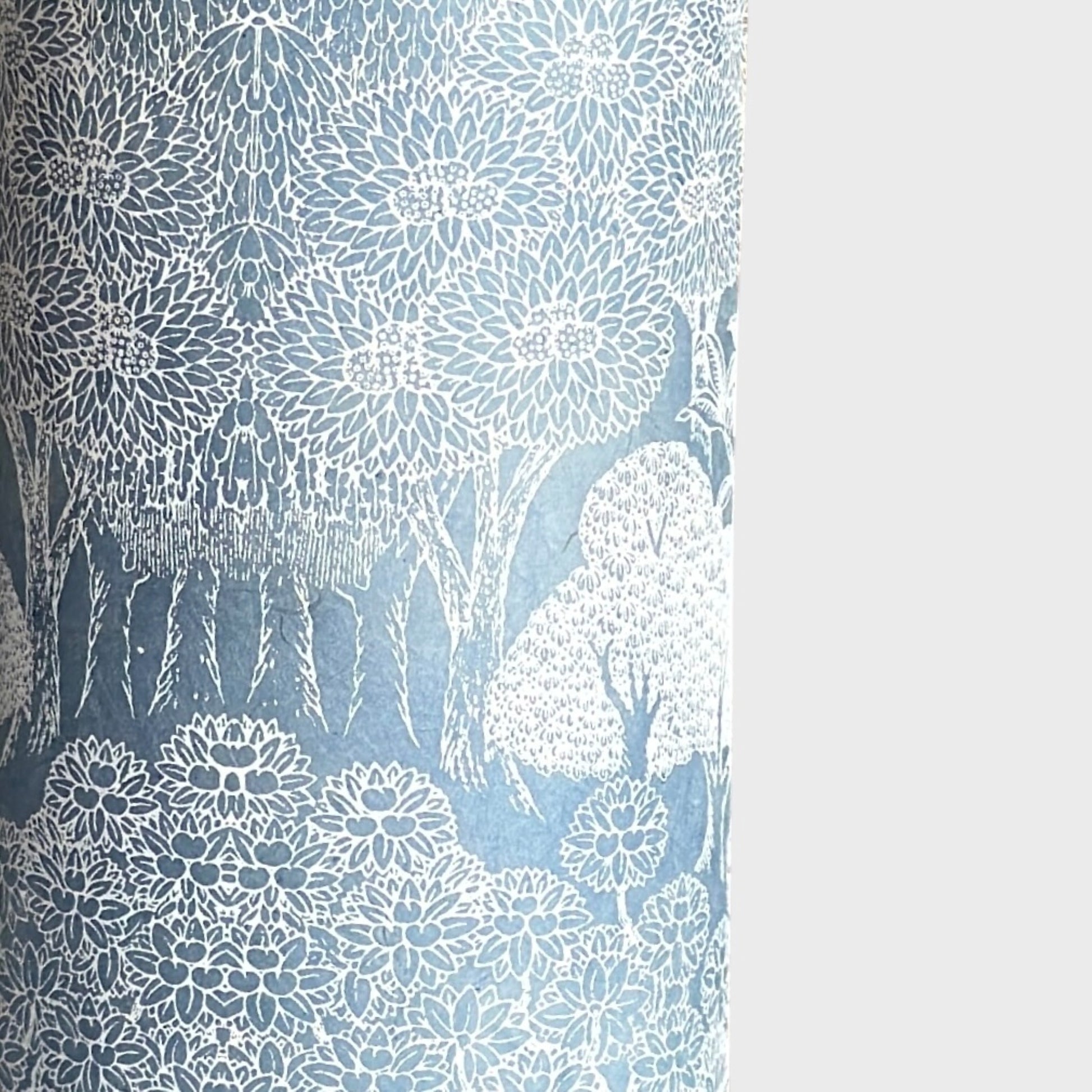 a sheet of Nepalese lokta paper in sky blue with a detailed pattern of trees and flowers screen printed in white