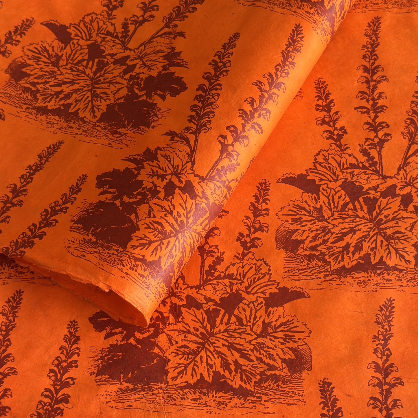 Nepalese handmade decorative lokta paper sheet with a Toile de Jouy style pattern of an agapanthus flower in burgundy screen printed on an orange lokta paper