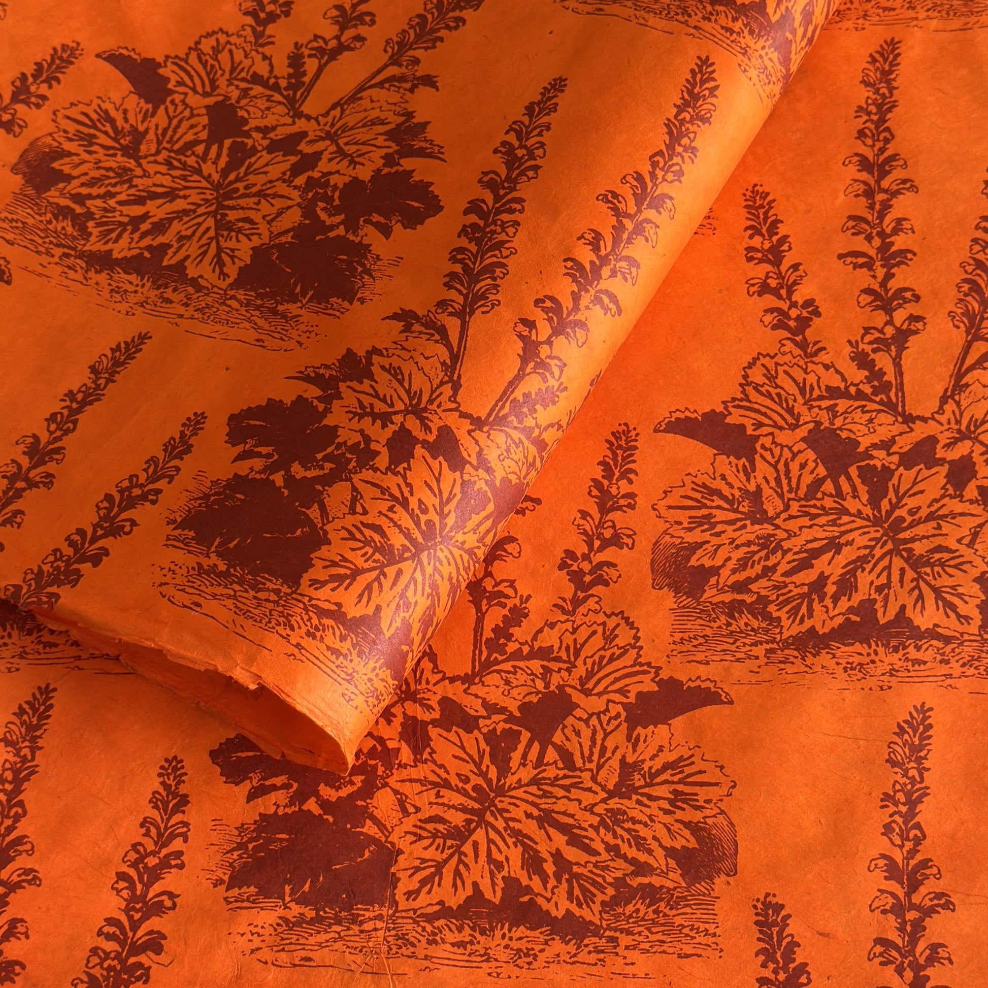 Nepalese handmade decorative lokta paper sheet with a Toile de Jouy style pattern of an agapanthus flower in burgundy screen printed on an orange lokta paper