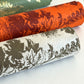 Nepalese handmade decorative lokta paper sheet with a Toile de Jouy style pattern of an agapanthus flower in burgundy screen printed on an orange lokta paper. Rolled with other designs