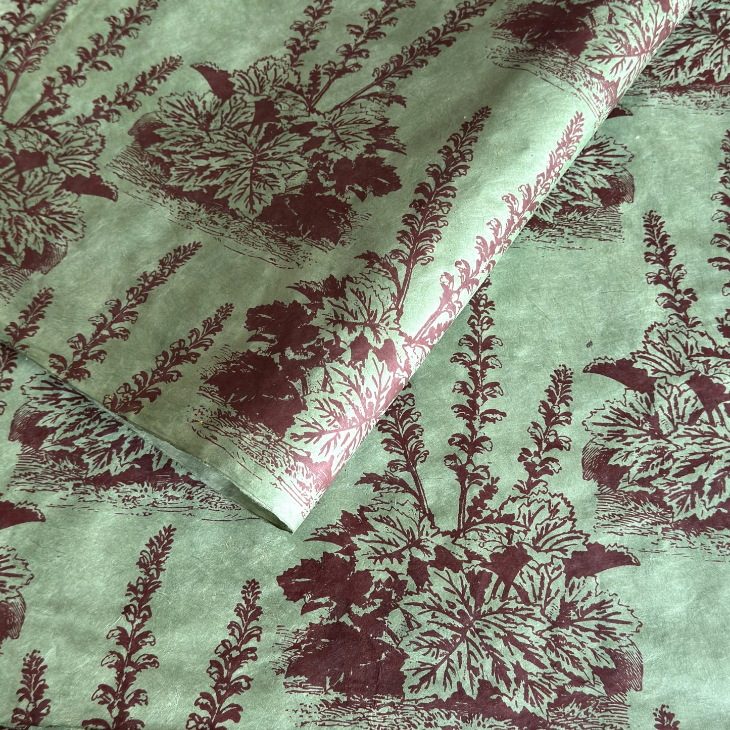 A Toile de Jouy style drawing of an agapanthus in aubergine screen-printed by hand on green lokta paper.