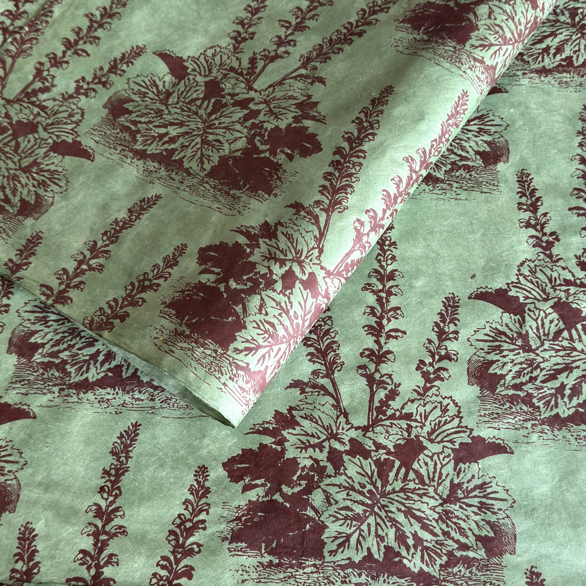 A Toile de Jouy style drawing of an agapanthus in aubergine screen-printed by hand on green lokta paper.