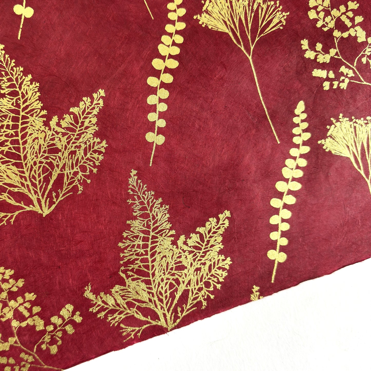 Nepalese handmade decorative lokta paper sheet with gold leaves screen printed on a burgundy red lokta paper, close up