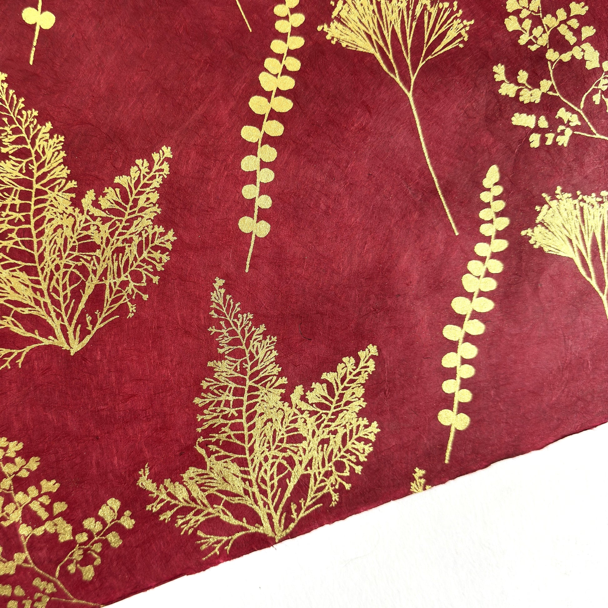 Nepalese handmade decorative lokta paper sheet with gold leaves screen printed on a burgundy red lokta paper, close up