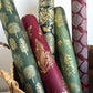 Nepalese handmade decorative lokta paper sheet with gold leaves screen printed on a burgundy red lokta paper, rolled with other designs