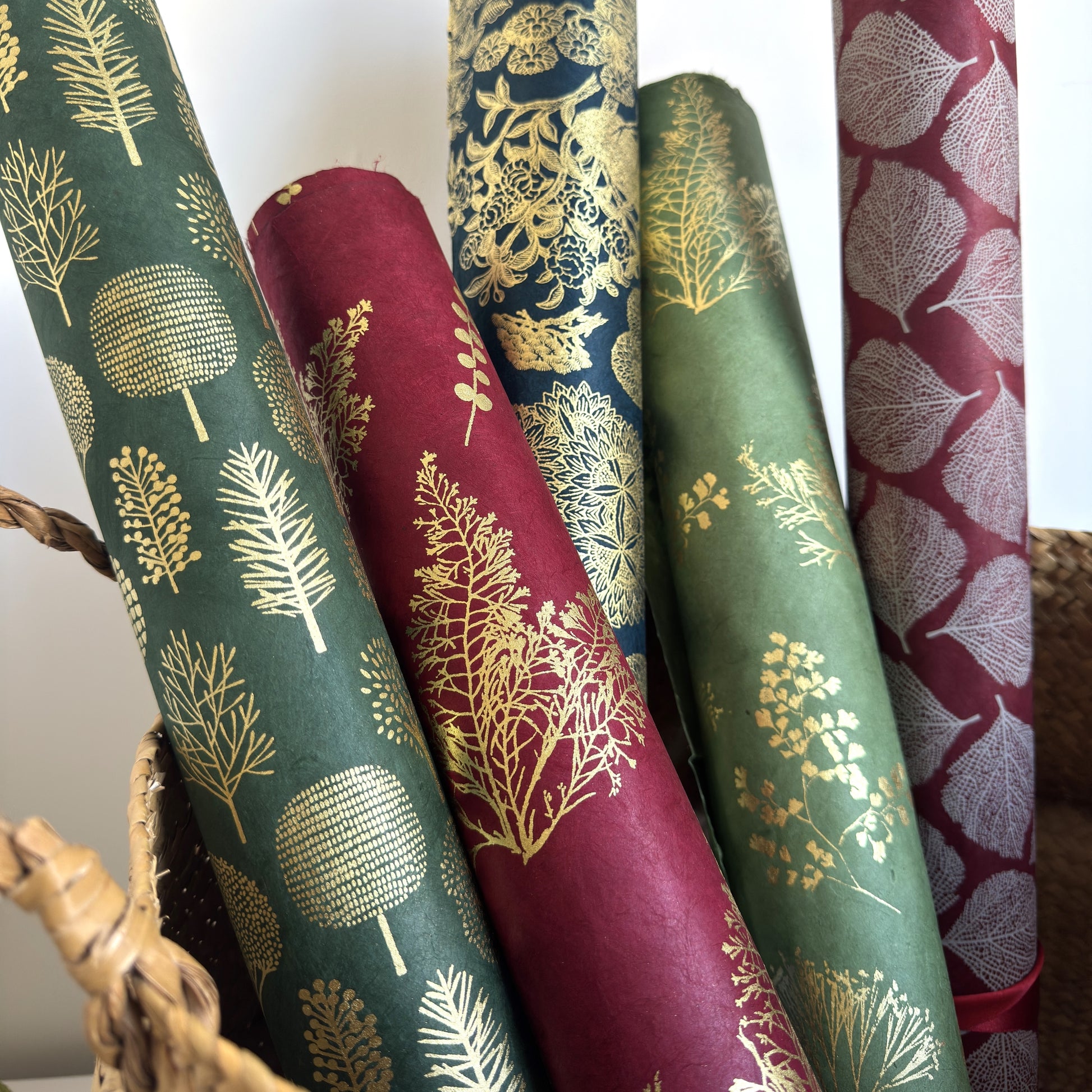 Nepalese handmade decorative lokta paper sheet with gold leaves screen printed on a burgundy red lokta paper, rolled with other designs