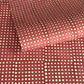 a sheet of Nepalese batik lokta paper in coral rose colour with a repeat white dot design. Pictured lightly rolled
