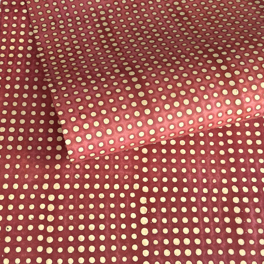 a sheet of Nepalese batik lokta paper in coral rose colour with a repeat white dot design. Pictured lightly rolled