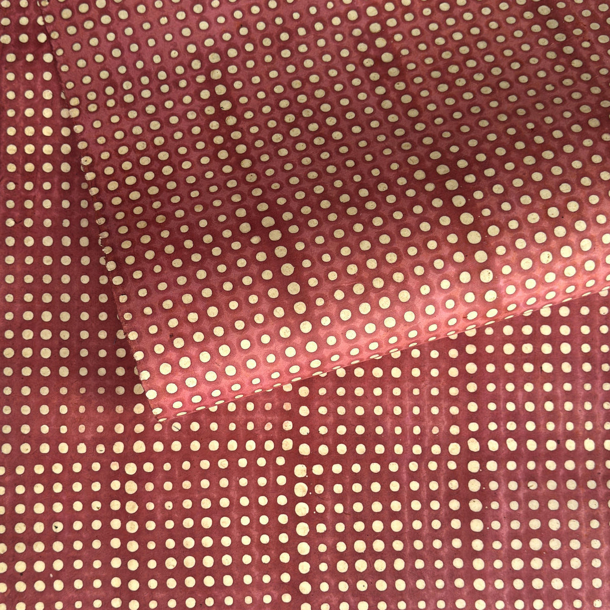 a sheet of Nepalese batik lokta paper in coral rose colour with a repeat white dot design. 