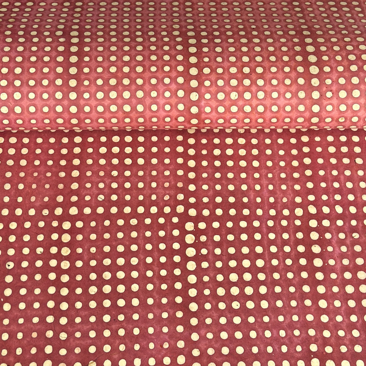 a sheet of Nepalese batik lokta paper in coral rose colour with a repeat white dot design. 