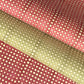 a sheet of Nepalese batik lokta paper in coral rose colour with a repeat white dot design. Pictured lightly folded alongside a sheet of the same design in sage green