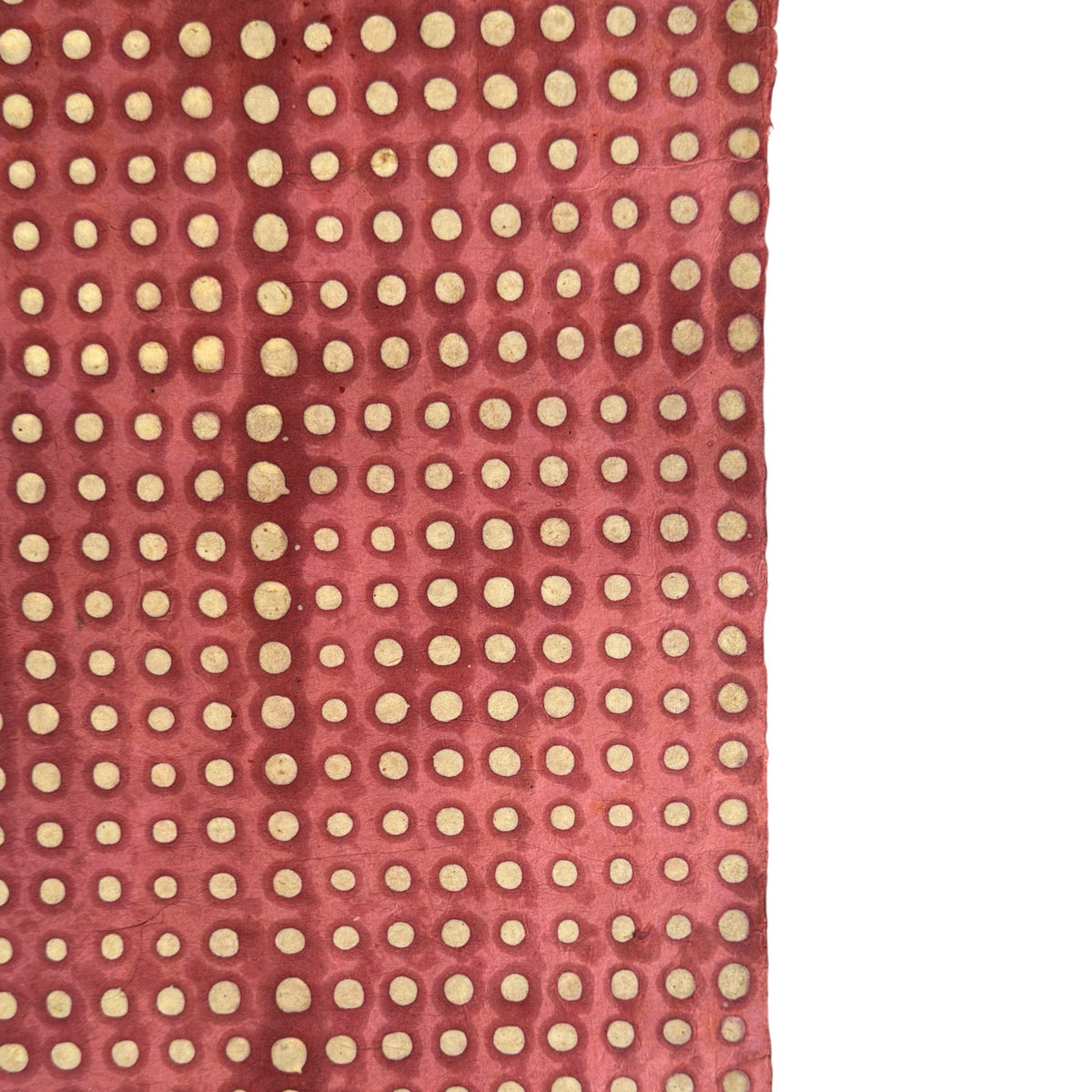 a sheet of Nepalese batik lokta paper in coral rose colour with a repeat white dot design. Close up