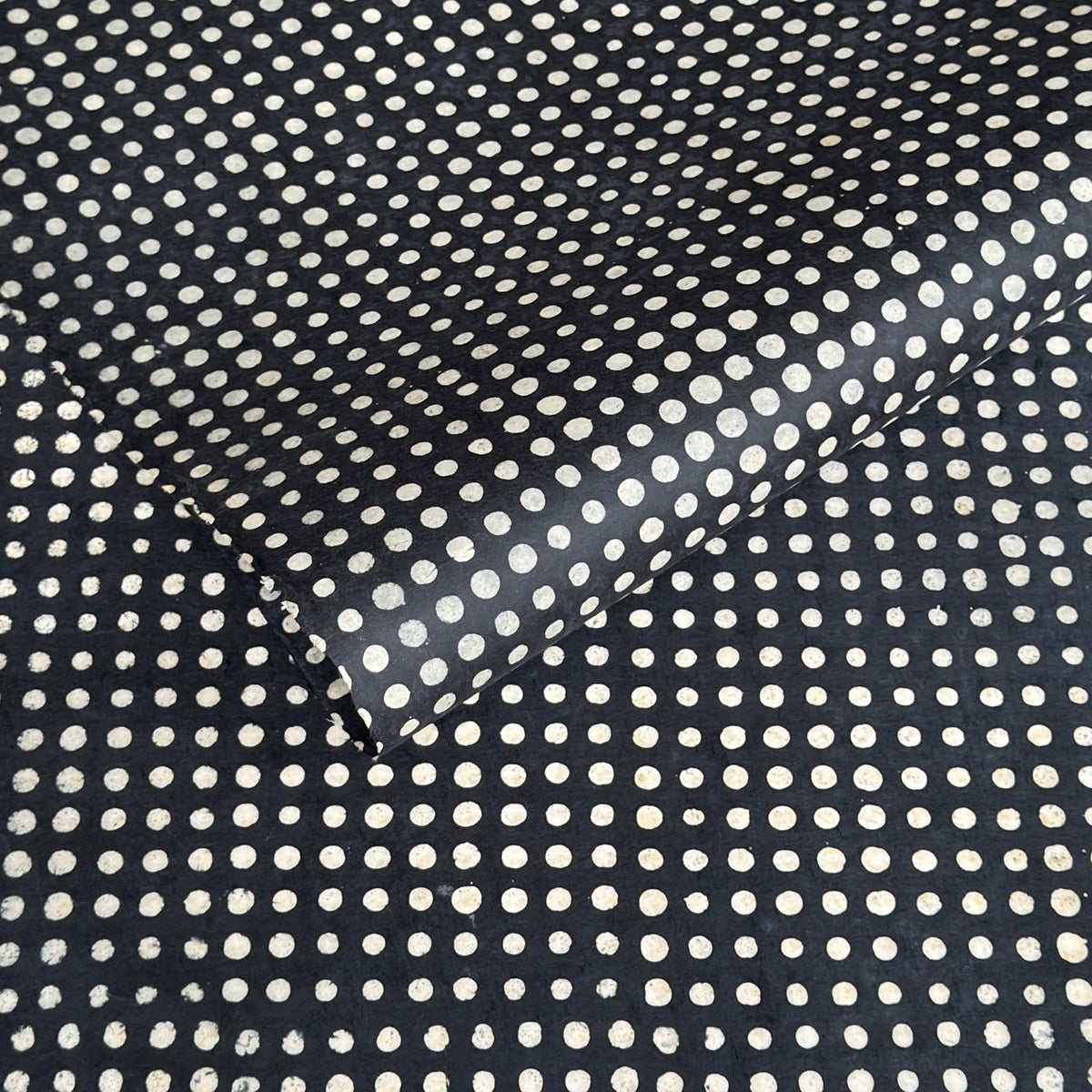 a sheet of black batik dyed Nepalese lokta paper with repeat design of white dots.  Pictured lightly folded