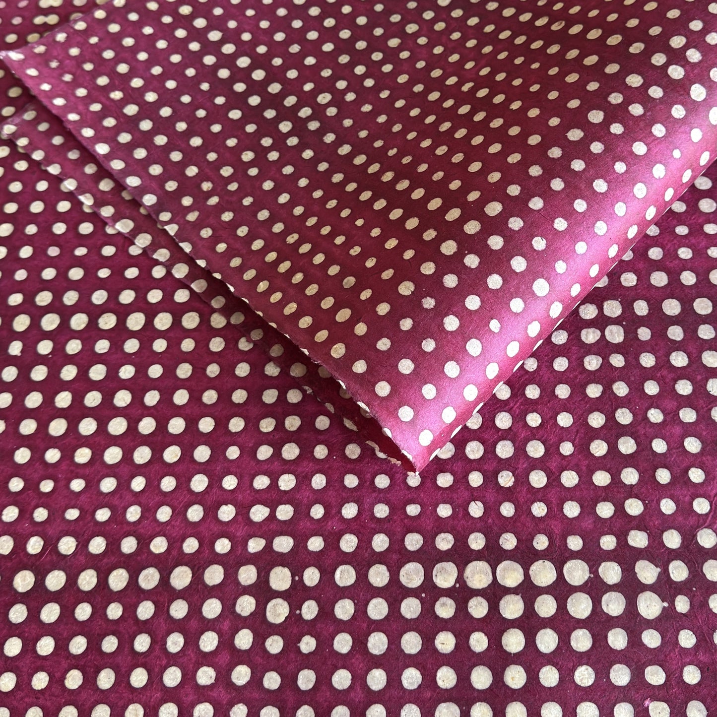 Nepalese handmade decorative lokta paper sheet with a pattern of white dots on burgundy red lokta paper.  Batik dyed using carved wooden blocks.