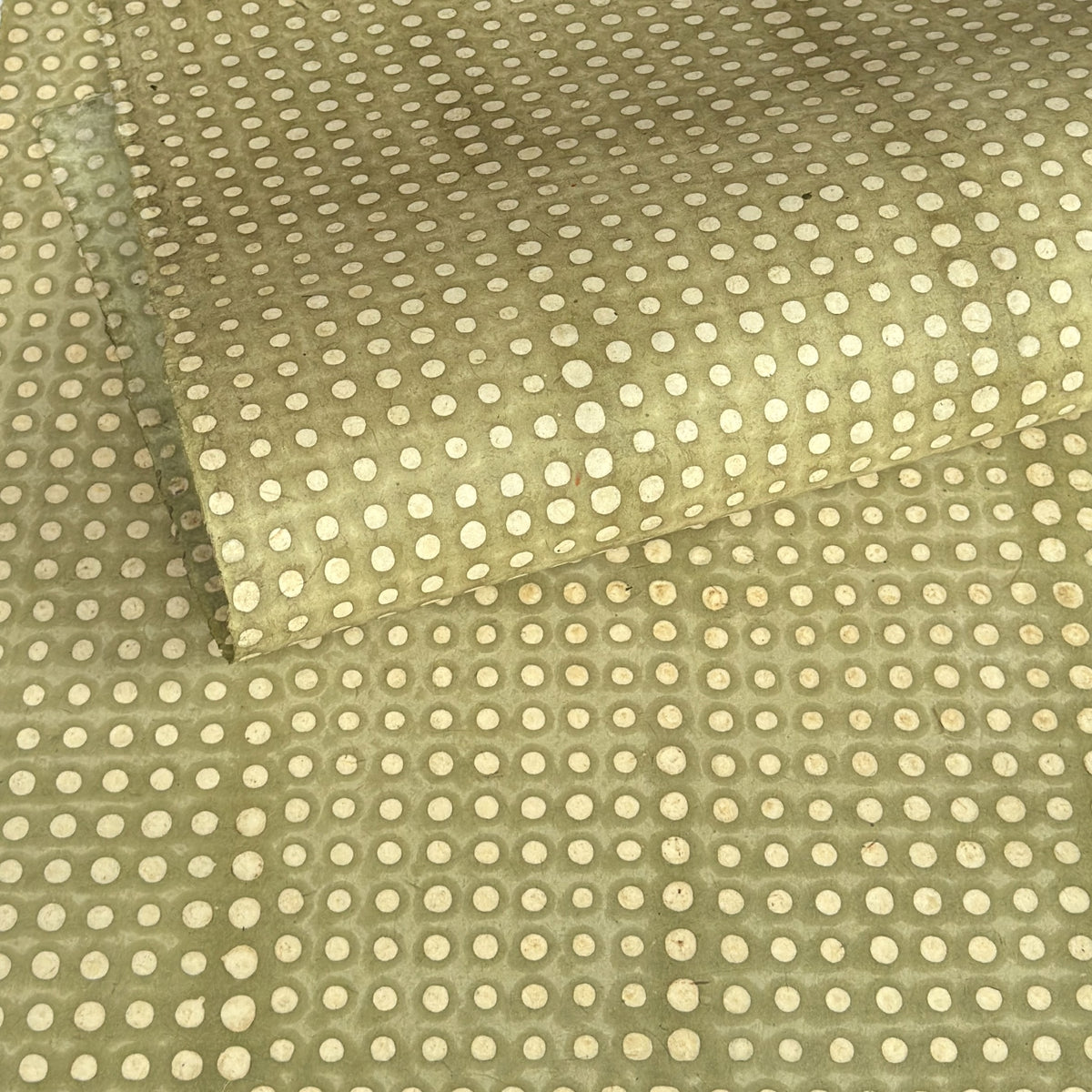 a sheet of Nepalese batik lokta paper in sage green with a repeat white dot design. Pictured gently rolled