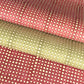 a sheet of Nepalese batik lokta paper in sage green with a repeat white dot design. Pictured lightly rolled with another paper in the red version of the same design