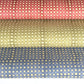 a sheet of Nepalese batik lokta paper in sky blue with a repeat white dot pattern.  Pictured rolled alongside the same designs in sage green and coral rose
