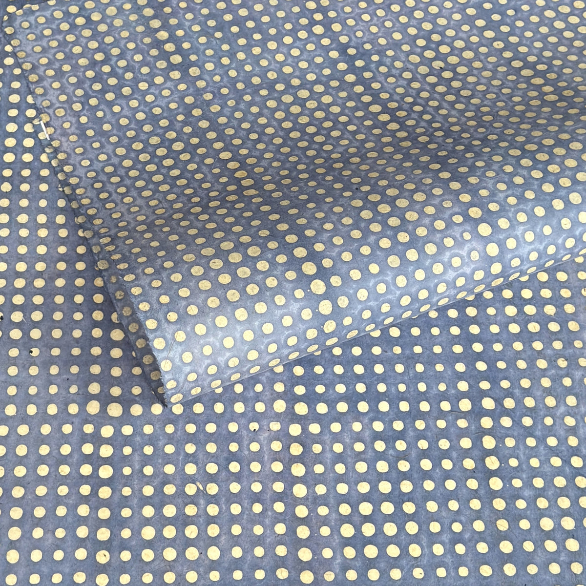 a sheet of Nepalese batik lokta paper in sky blue with a repeat white dot pattern. Pictured lightly rolled