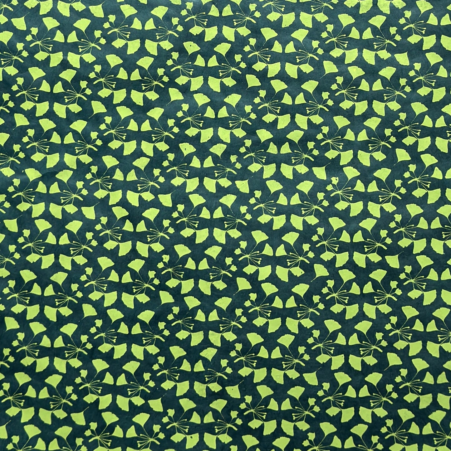 a sheet of lokta paper with a green abstract gingko design on dark green paper