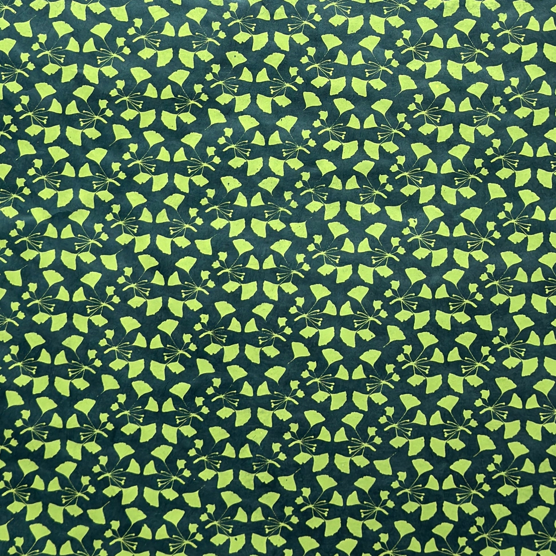 a sheet of lokta paper with a green abstract gingko design on dark green paper