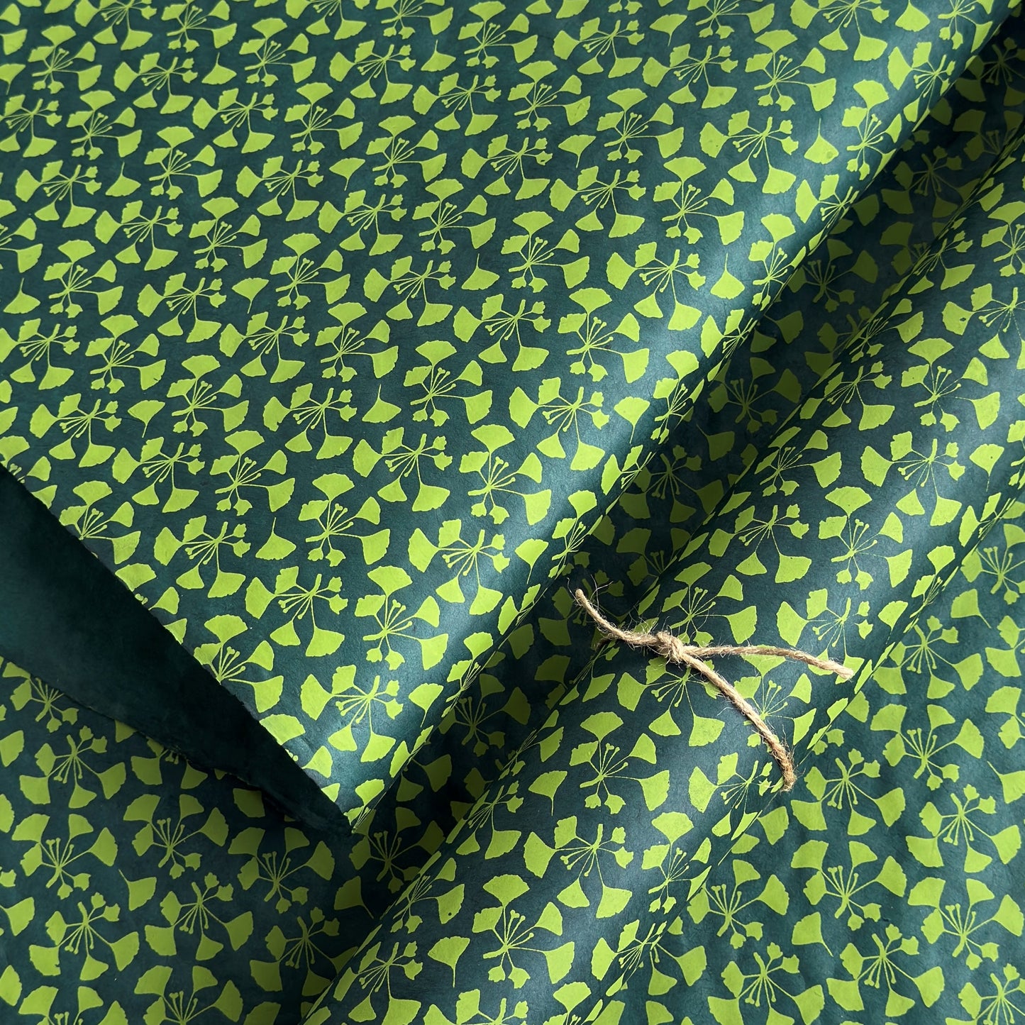 a sheet of lokta paper with a green abstract gingko design on dark green paper