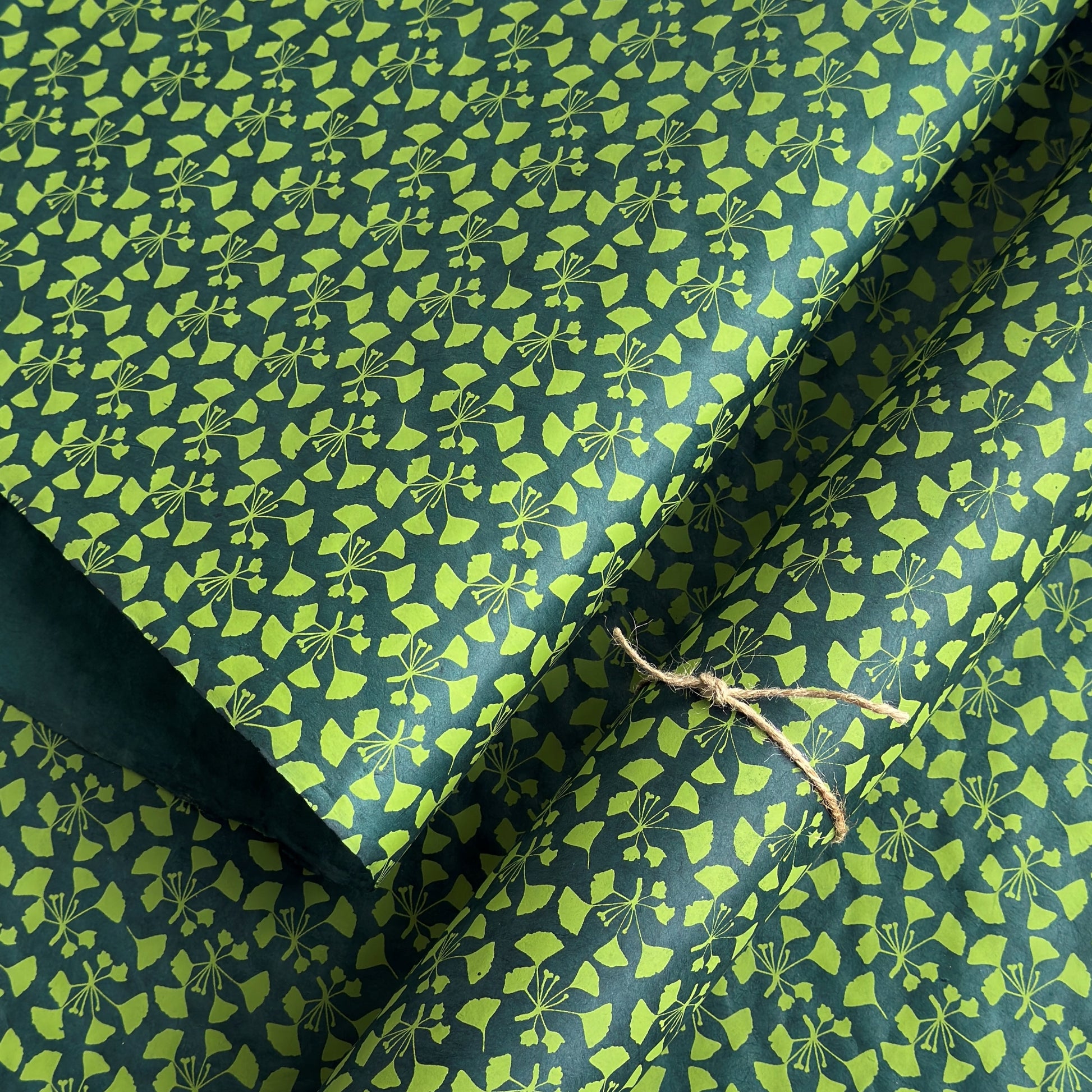 a sheet of lokta paper with a green abstract gingko design on dark green paper