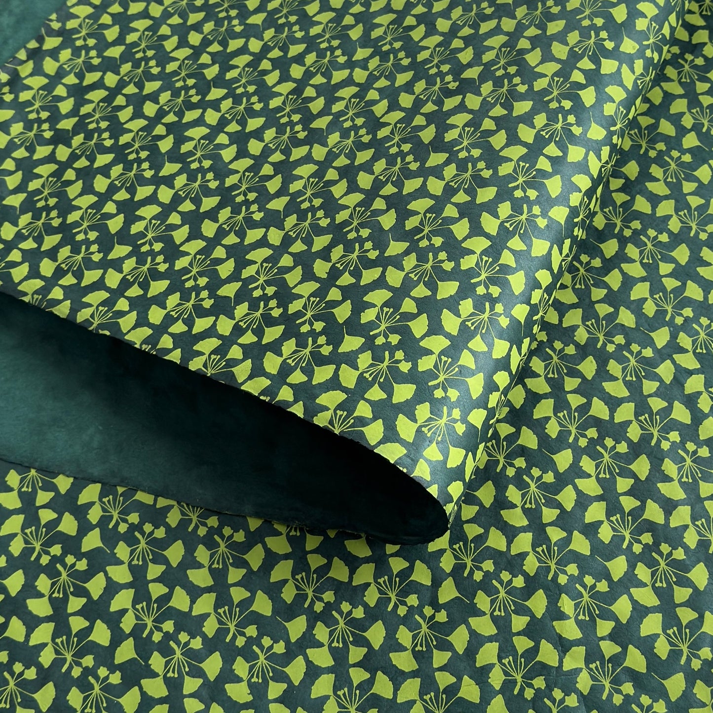 a sheet of lokta paper with a green abstract gingko design on dark green paper