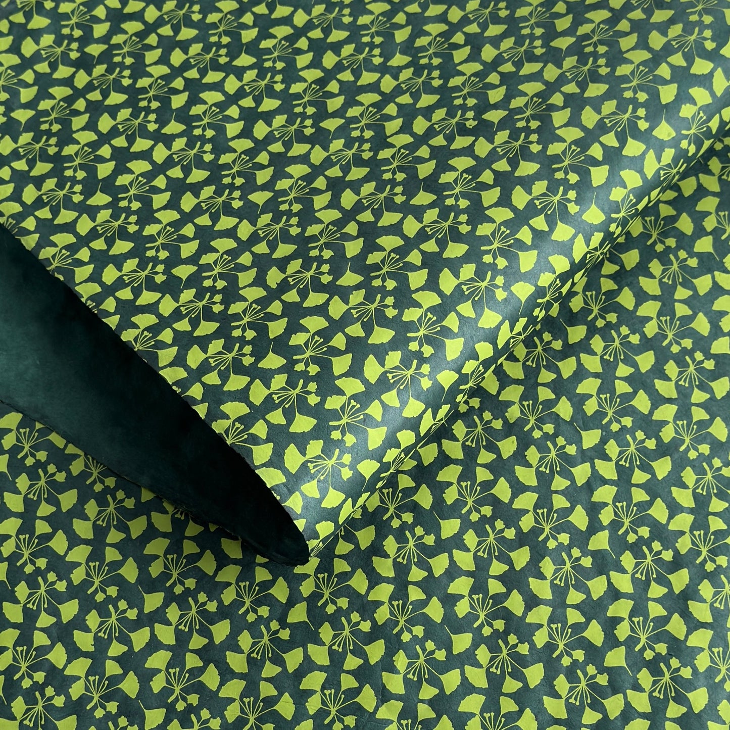 a sheet of lokta paper with a green abstract gingko design on dark green paper