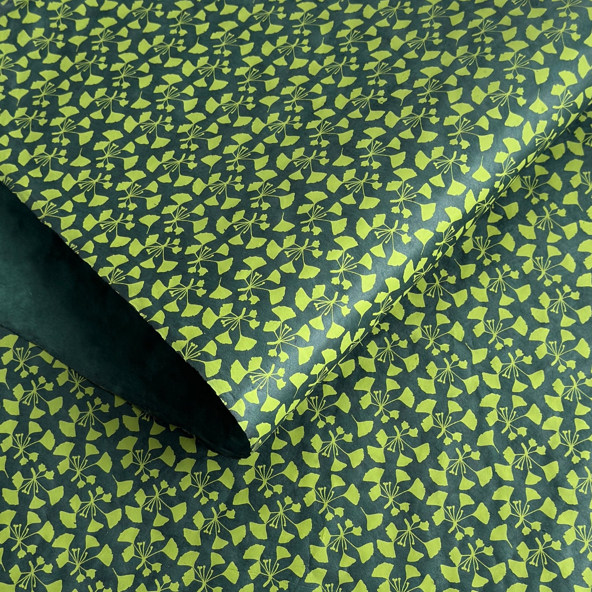 a sheet of lokta paper with a green abstract gingko design on dark green paper