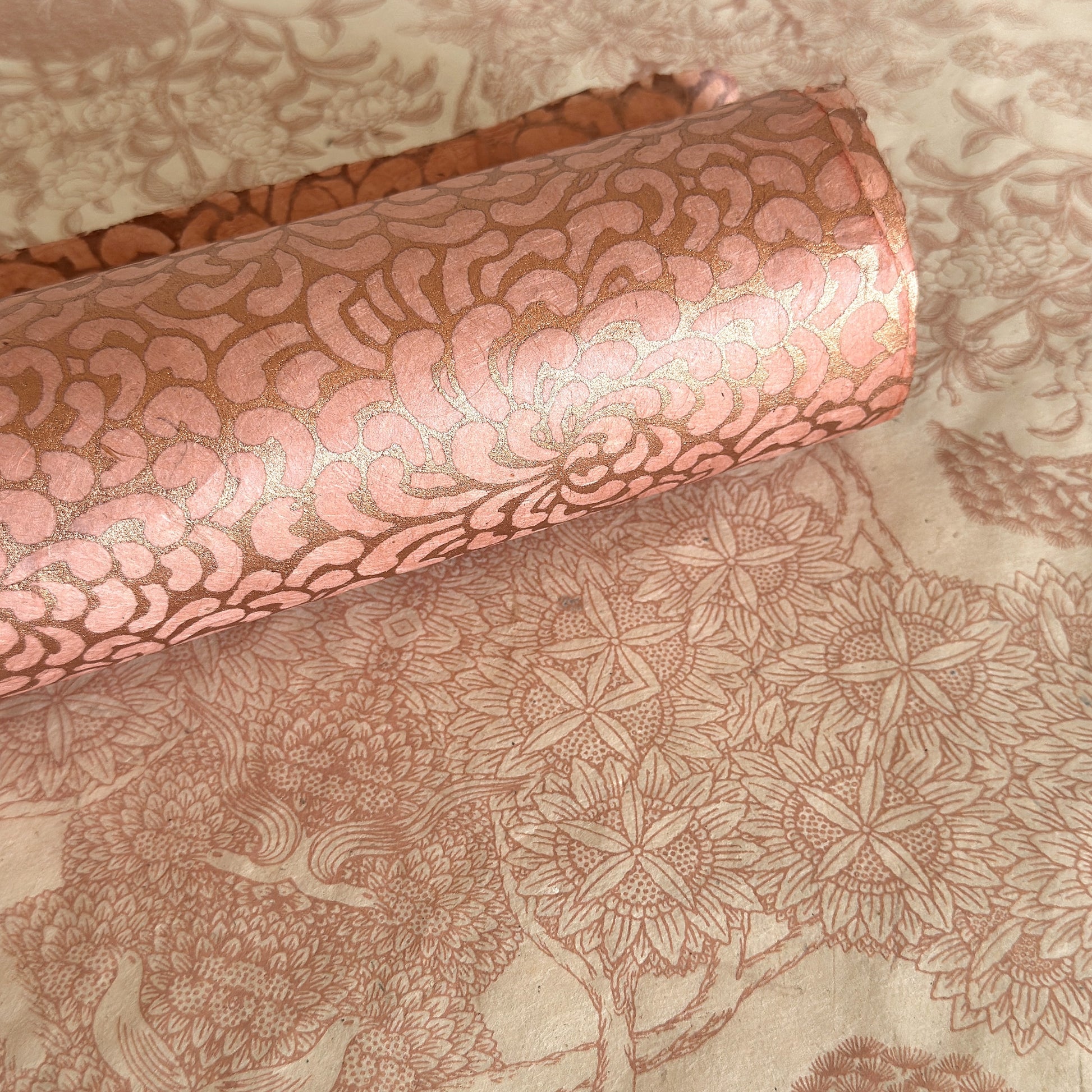 Nepalese handmade decorative lokta paper sheet with a metallic copper floral print screen printed on a blush pink lokta paper. Pictured rolled