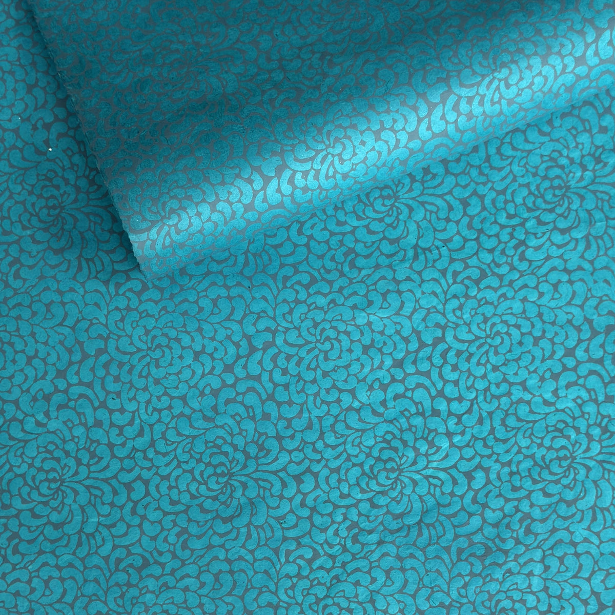 a sheet of Nepalese lokta paper screen printed with a repeat floral pattern in dark grey/blue on a bright teal lokta paper